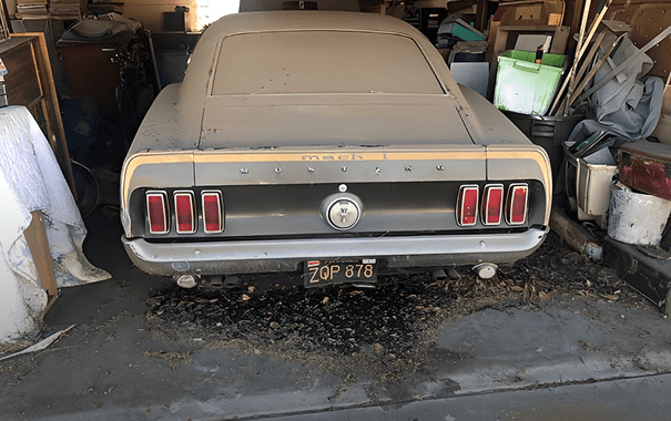 Dusty vintage car in cluttered garage.
