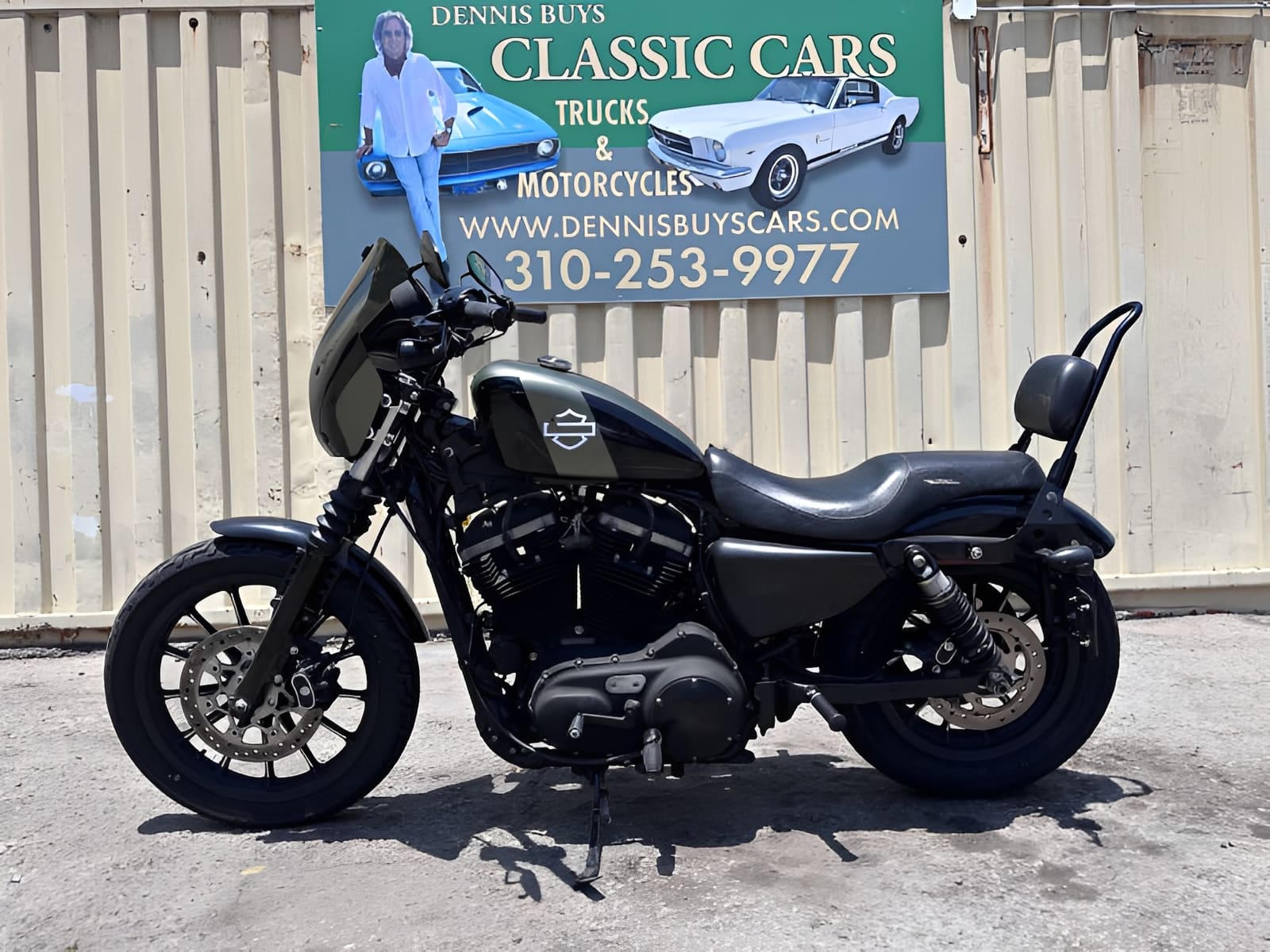 Black motorcycle in front of classic cars sign.