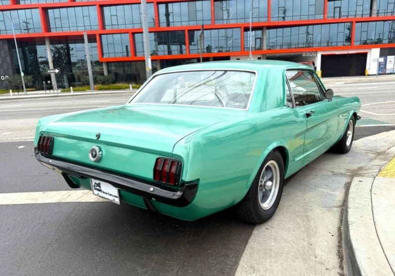 Green vintage car parked near modern building.