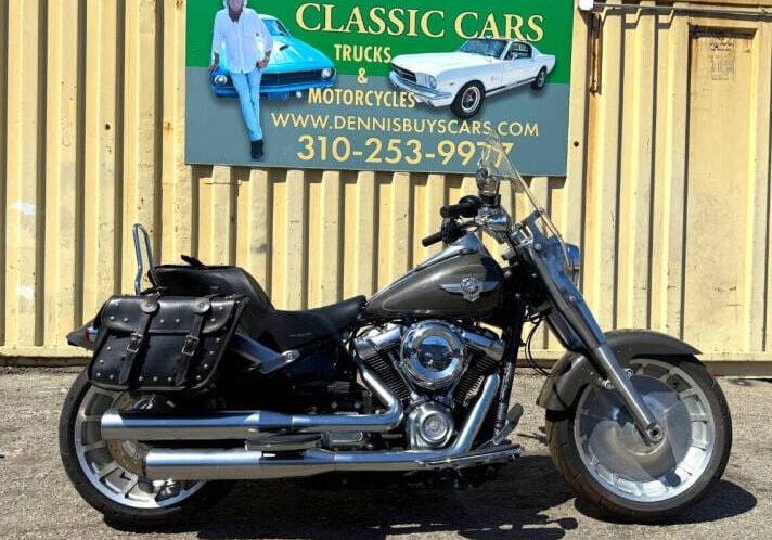 Motorcycle parked in front of classic cars sign.
