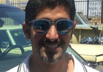 Man wearing sunglasses, smiling in sunny area.