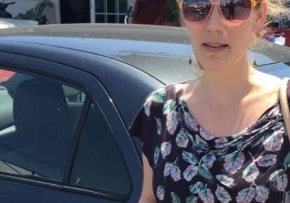 Woman standing beside a parked car.