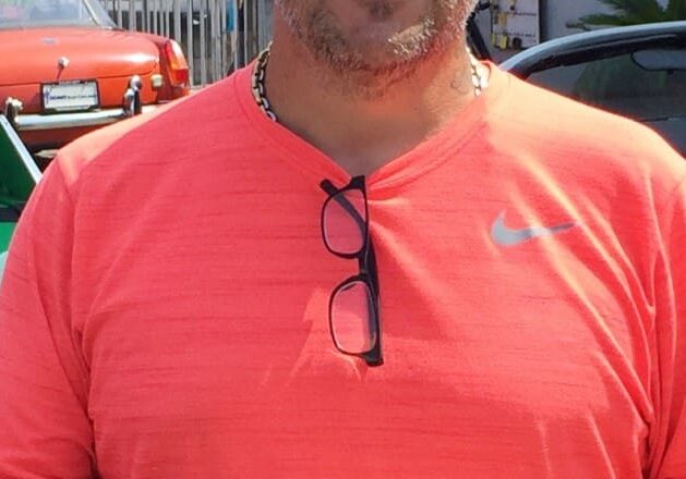 Man in orange shirt with cars behind.