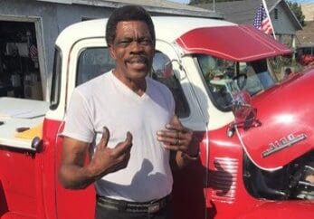 Man smiling beside a vintage red truck.