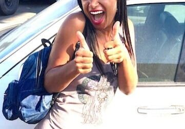 Woman smiling with thumbs up by car.
