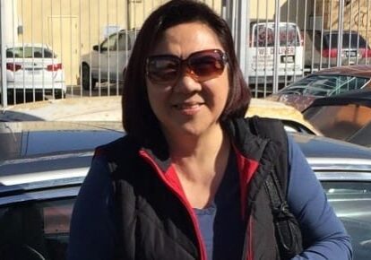 Woman wearing sunglasses standing by a car.
