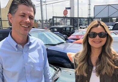 Smiling man and woman standing near cars.