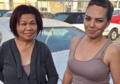 Two women standing in front of cars.
