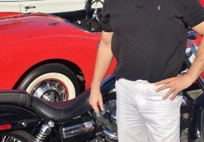 Man standing between motorcycle and vintage car.
