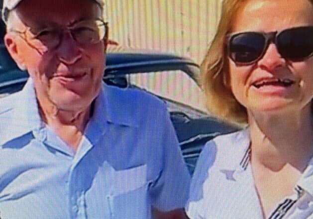 Elderly man and woman posing with car.