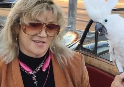Woman holding a white cockatoo outside.