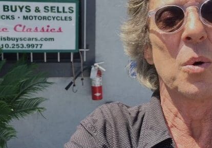 Man in sunglasses in front of business sign.